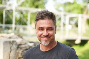 Man with beard and grey shirt smiling outside