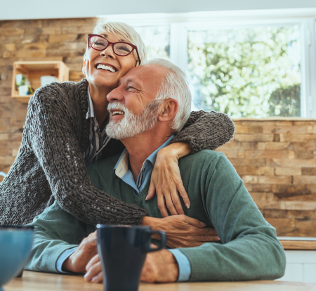 Smiling senior man and woman hugging while sitting at their coffee table
