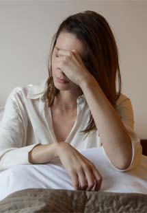 Woman sitting in bed rubbing forehead in frustration