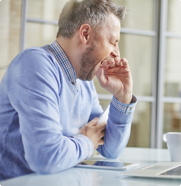 Man in light blue sweater covering his mouth while yawning