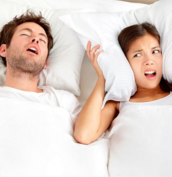 Woman covering her ears with pillow next to snoring man