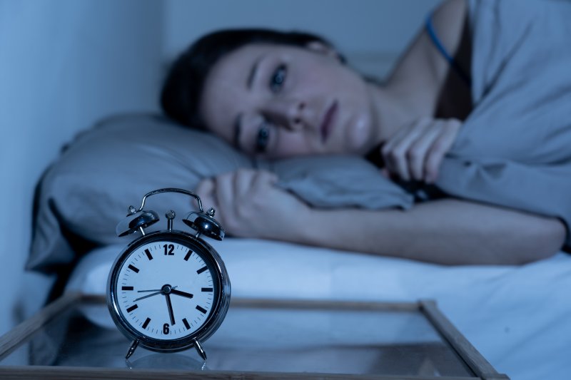 Anxious woman lying in bed staring at alarm clock