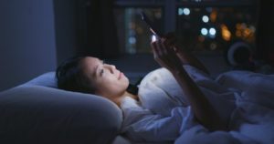 young woman using phone in bed